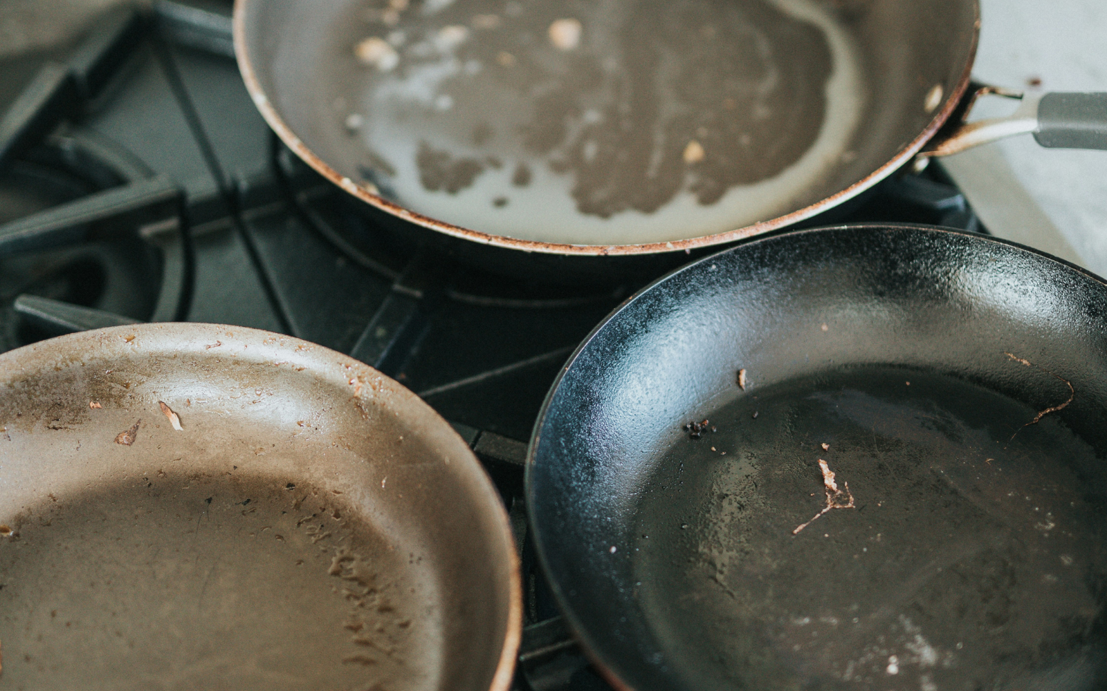 variety of frypans including stainless steel saucepan and cast iron skillet heating on a gas stovetop.
