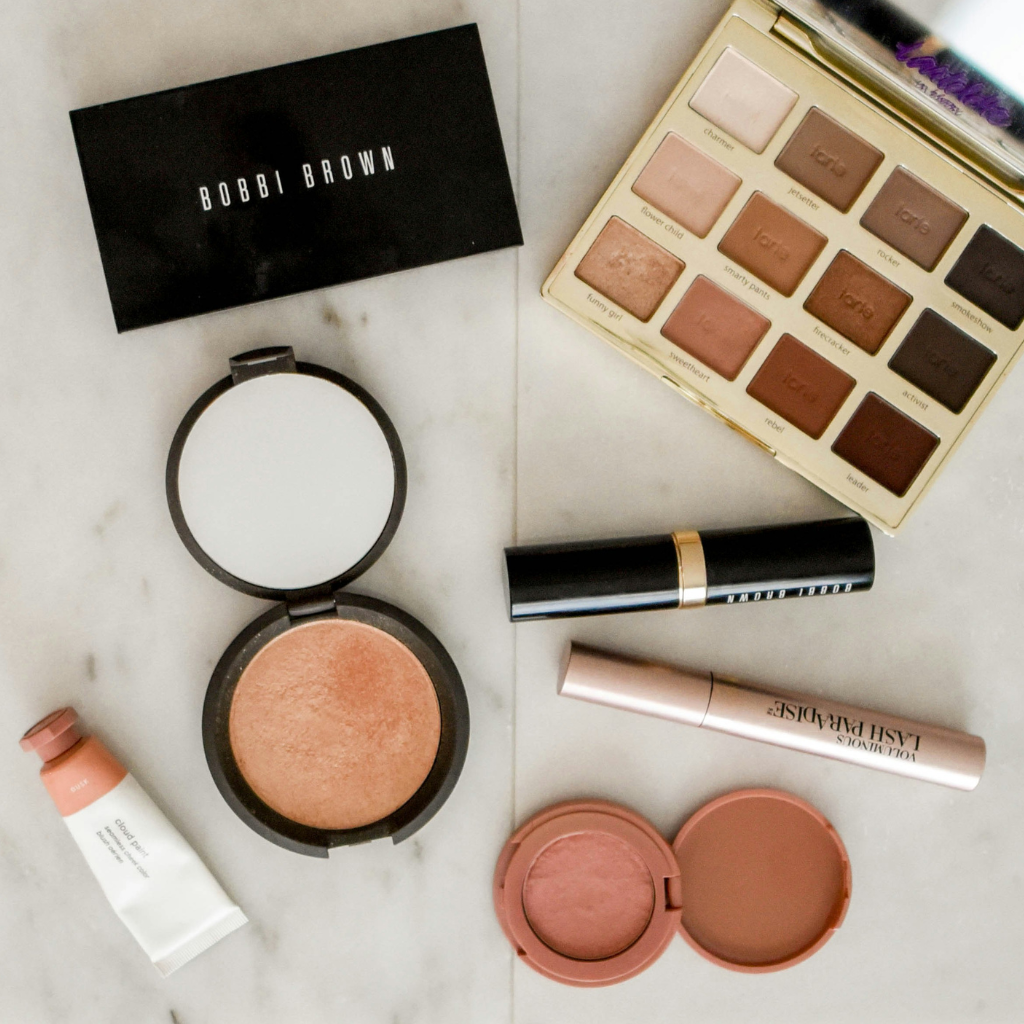 Makeup products including a Bobbi Brown compact, blush, and eyeshadow palette on a marble surface.