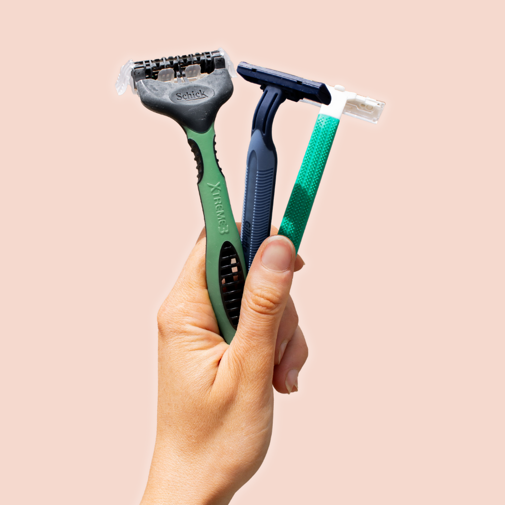Hand holding three razors against a beige background