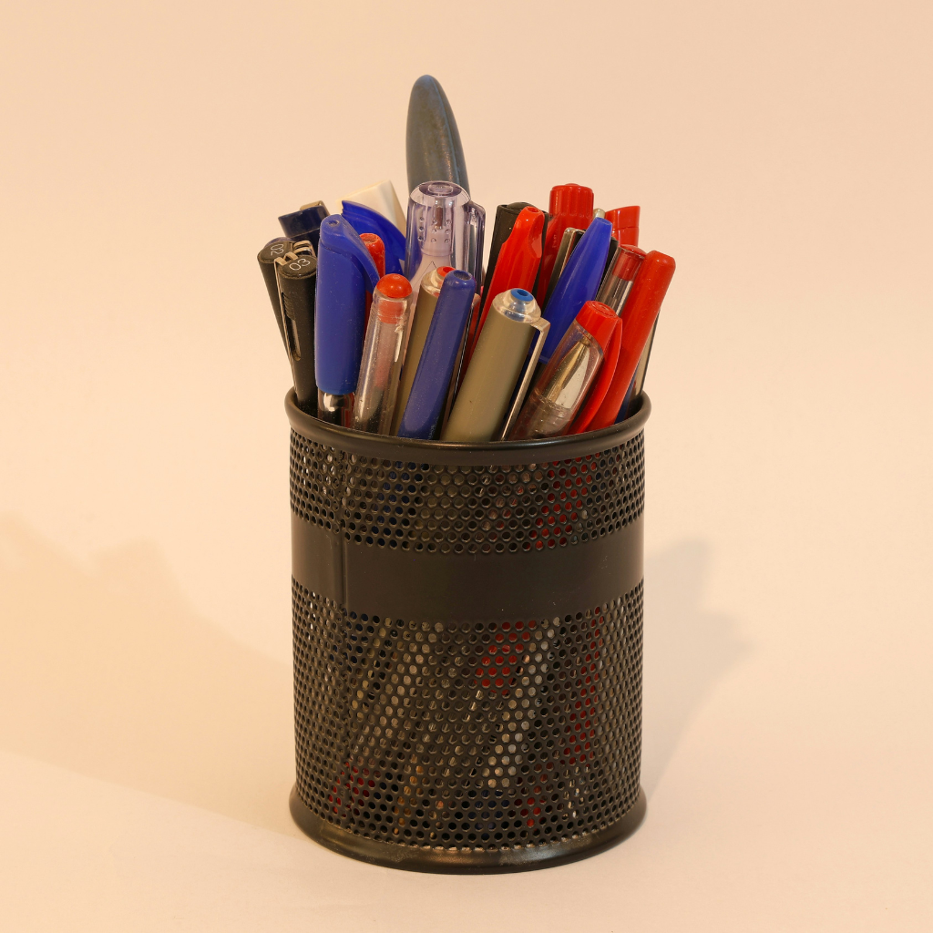 Black mesh pen holder with various pens on a beige background